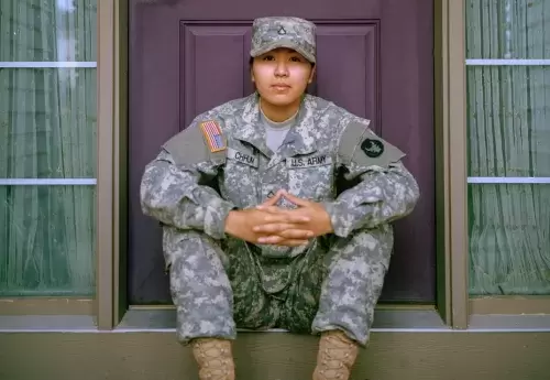 A feminine presenting soldier sitting on a porch in front of a purple door.