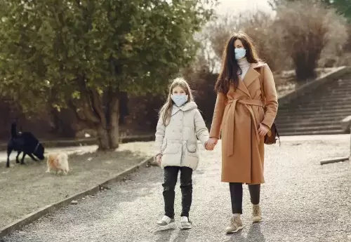 Woman walking daughter to school with face mask.