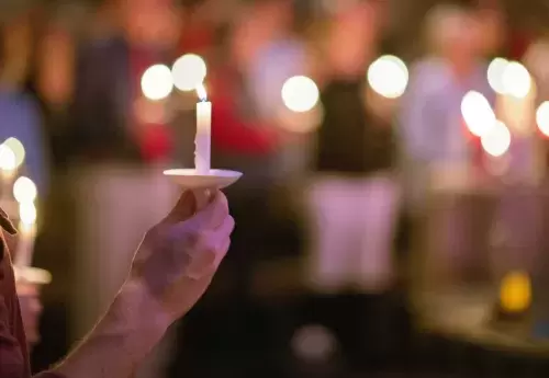 hand holds a candle with many other hands also holding candles