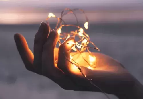 hand holds knotted string of lights on a beach