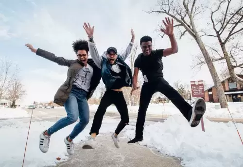 three students jump in air in front of snowy landscape